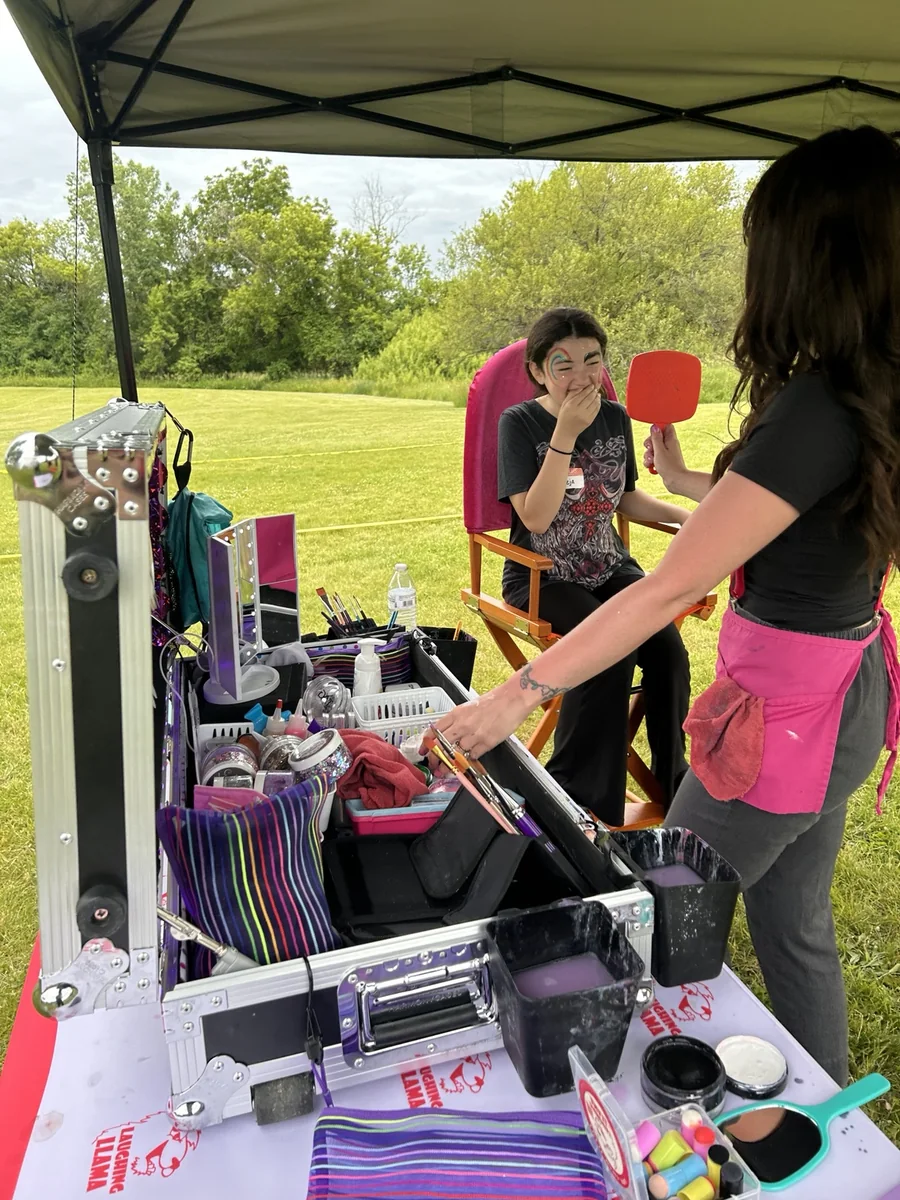 Mel sharing a finished face paint reveal with a guest outdoors.