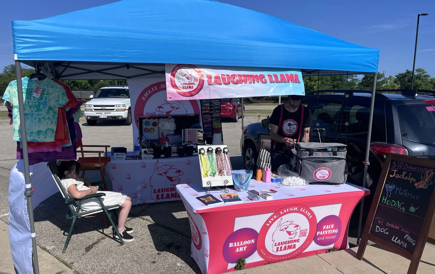 Outdoor Laughing Llama event setup with tent banner and bright merch.