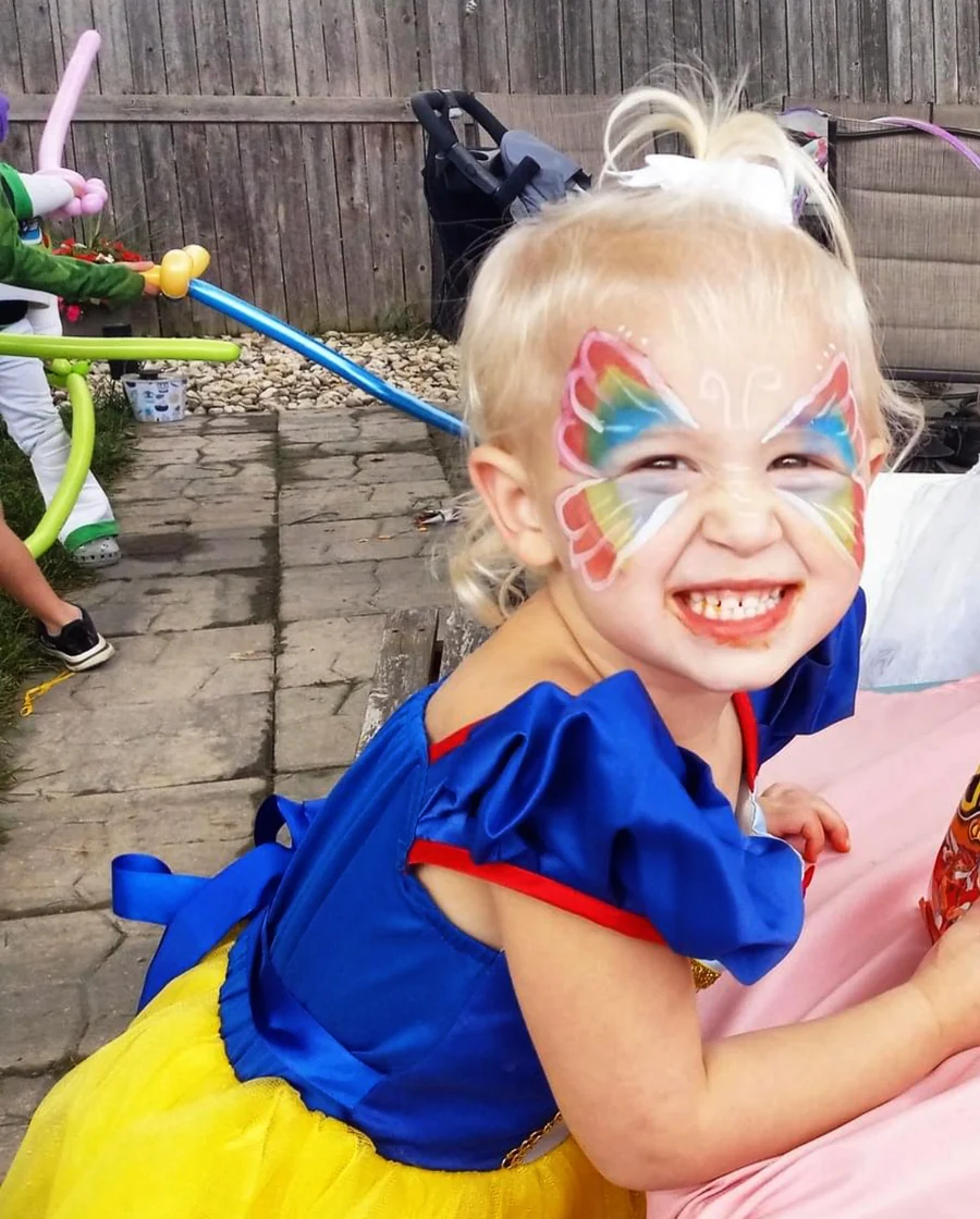 Smiling child with rainbow butterfly face paint.