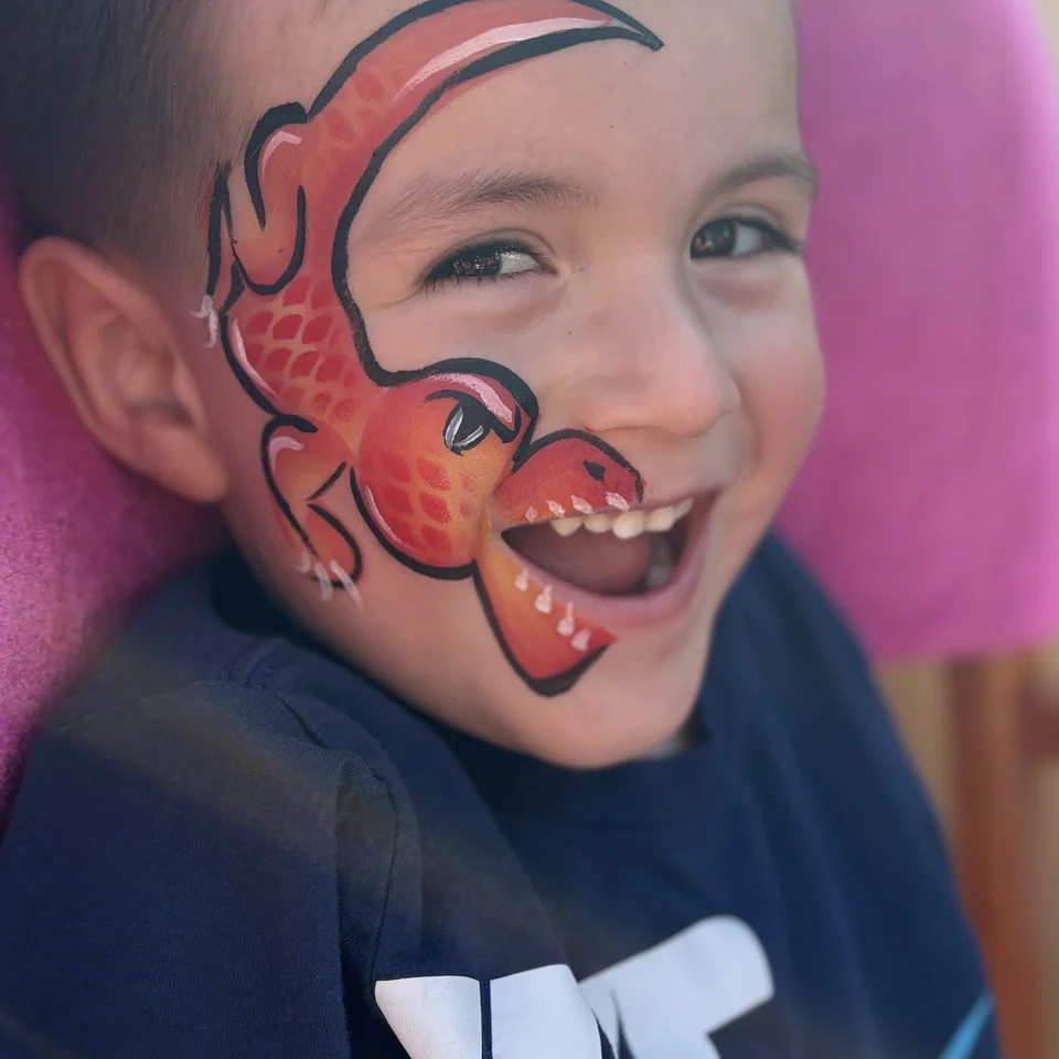Close-up of a child laughing with dinosaur face paint.