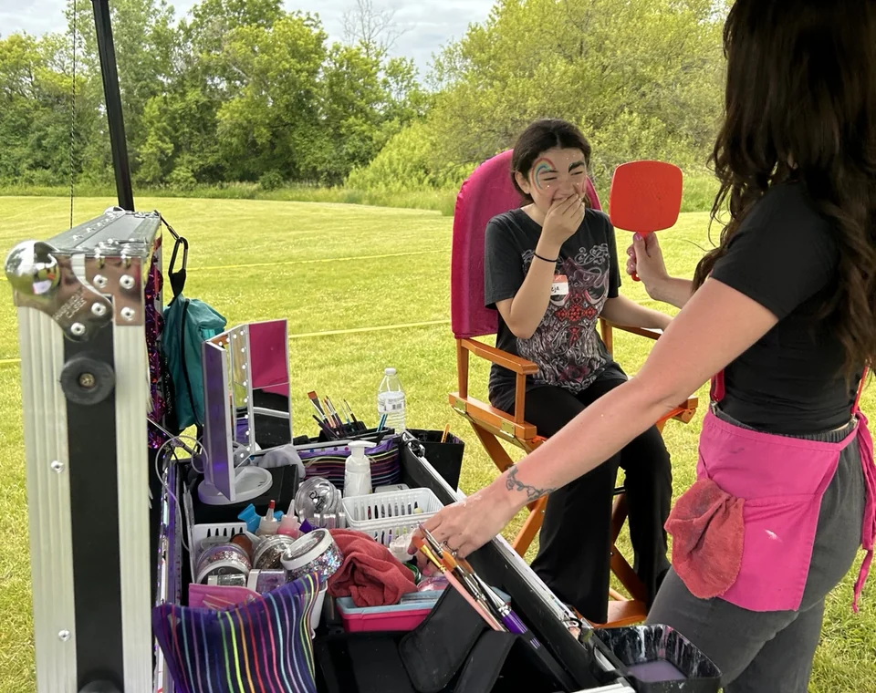 Mel showing a guest their finished face paint in a hand mirror.