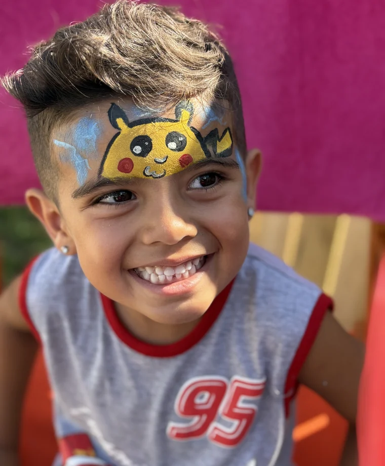 Smiling child with bright Pikachu-inspired face paint.