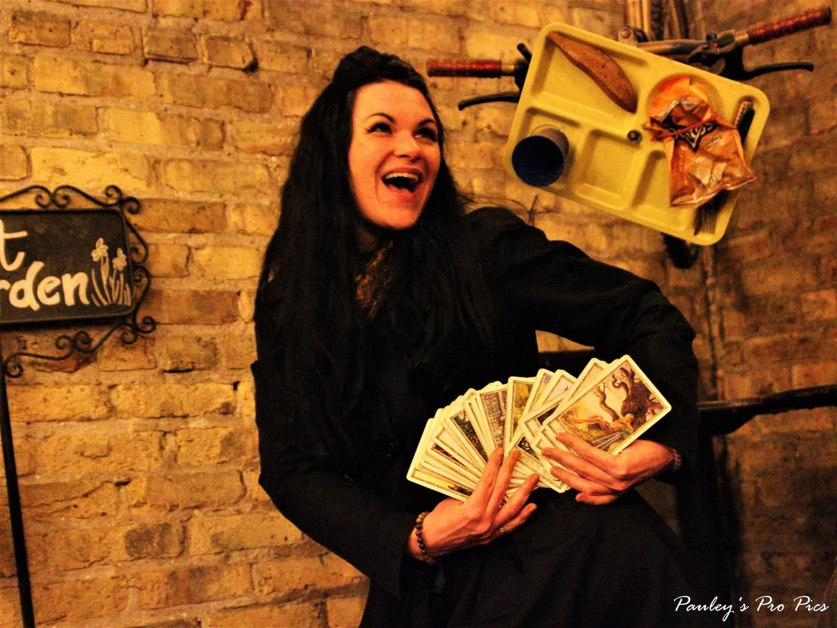 Mel seated at a tarot table with cards spread out.
