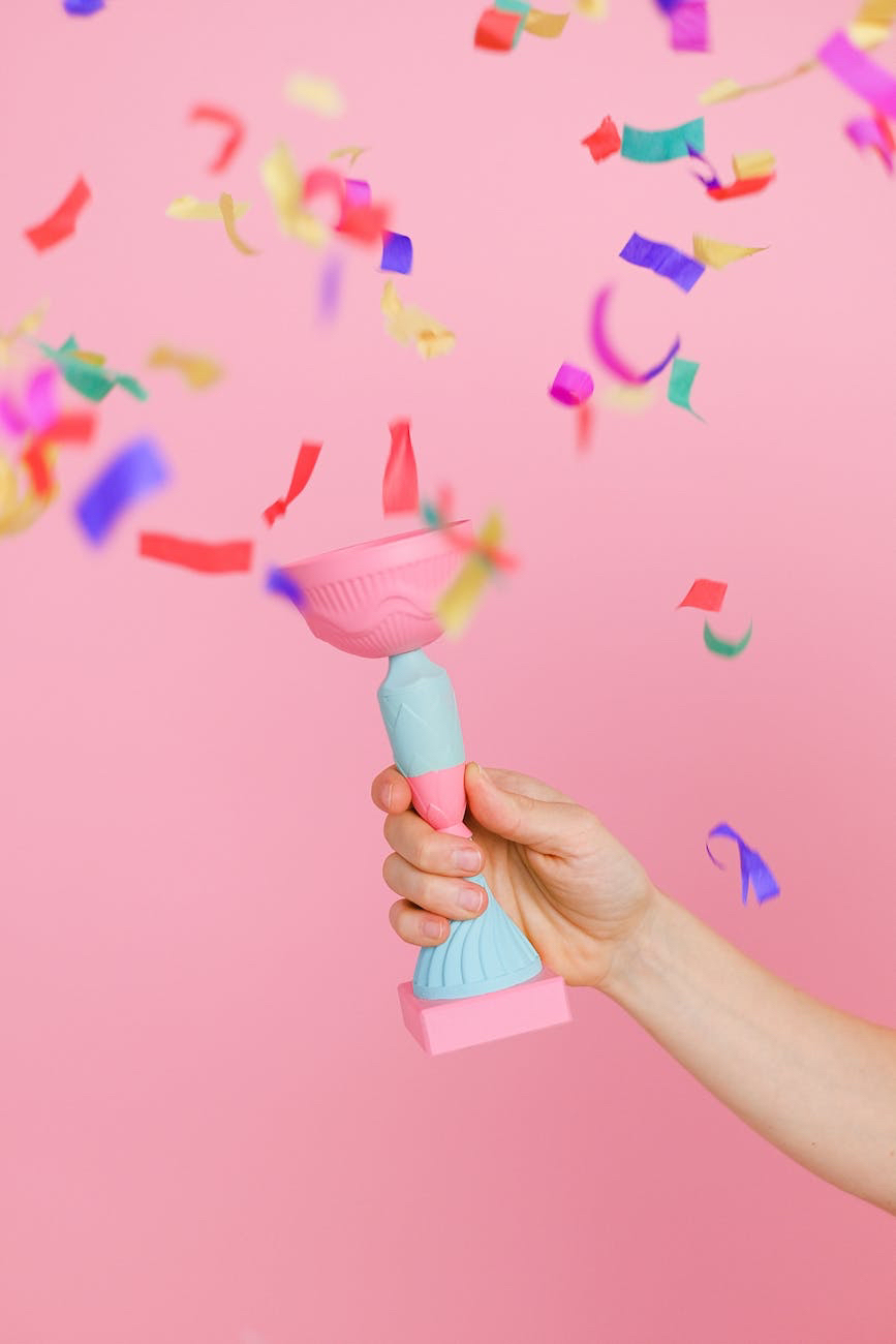 A hand holds up a plastic chalice as confetti falls around, the colors are pastels